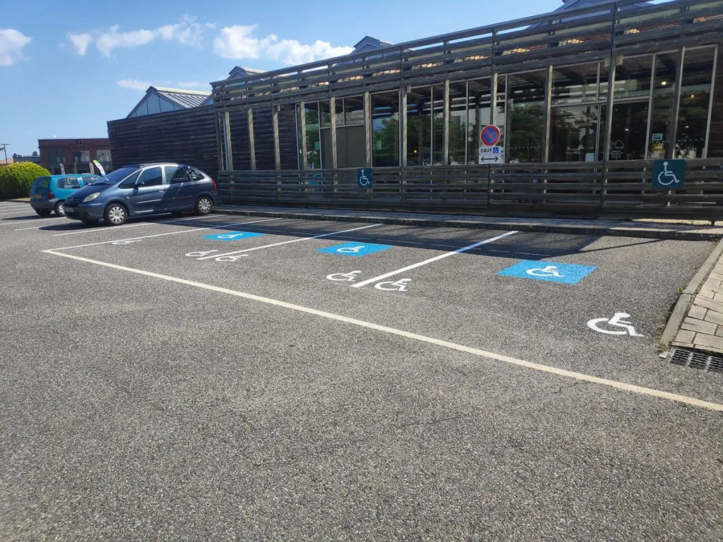 Plusieurs places de stationnement PMR avec pictogrammes bleus devant un commerce