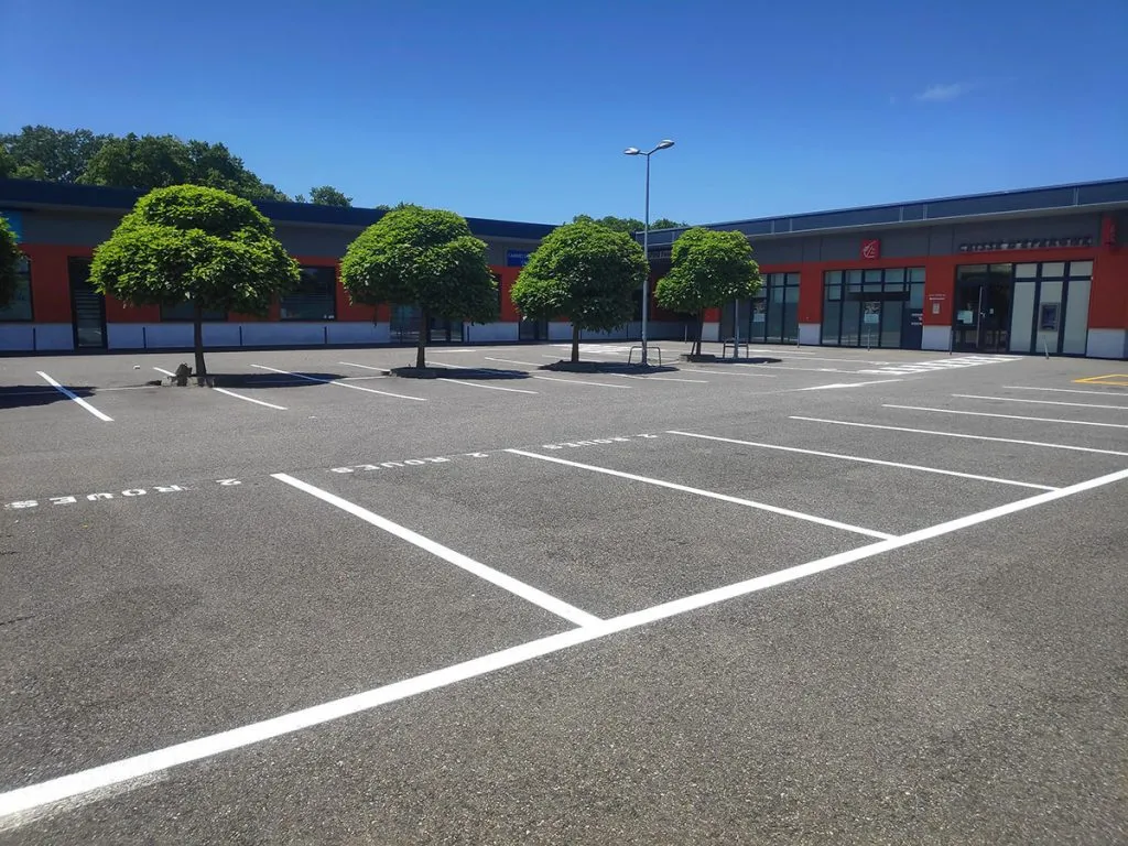 Parking de zone commerciale avec emplacements blancs fraîchement tracés devant un bâtiment