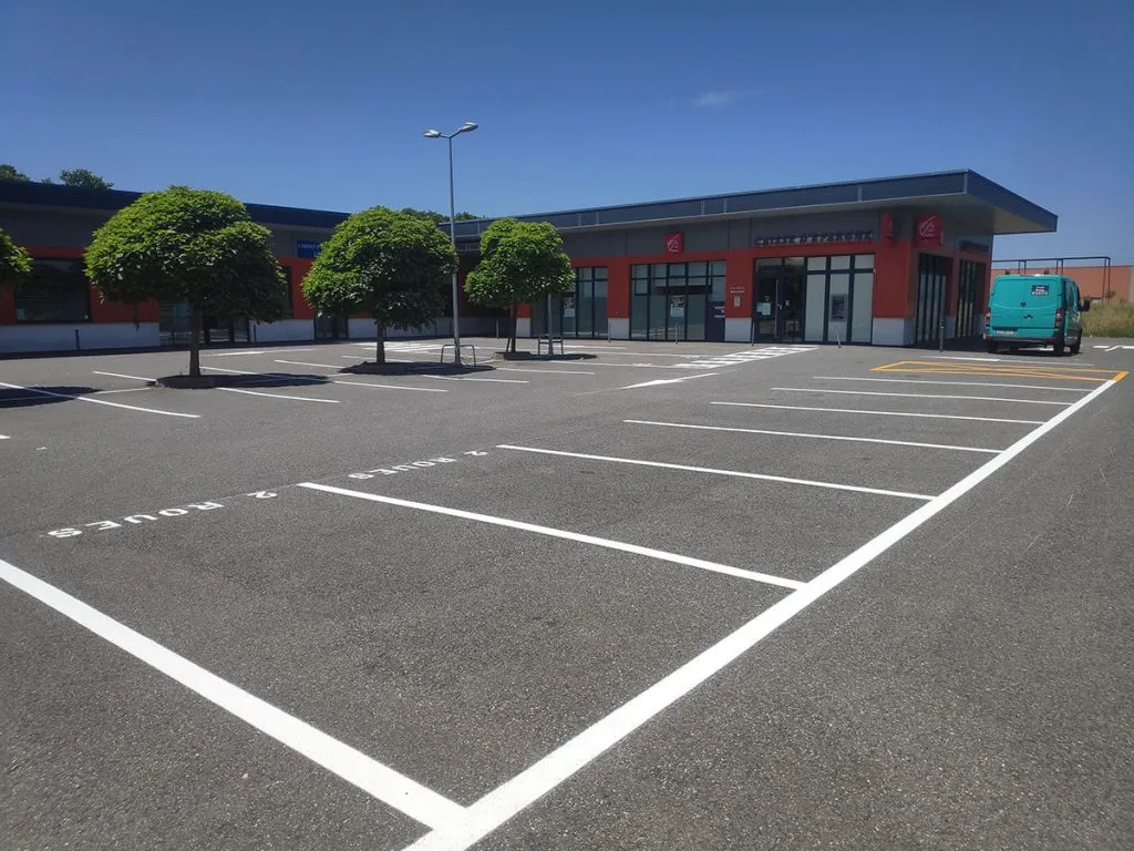 Parking professionnel rénové avec emplacements blancs alignés devant un bâtiment tertiaire