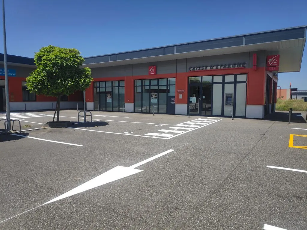 Parking professionnel avec passage piéton, flèches et emplacements blancs devant un bâtiment