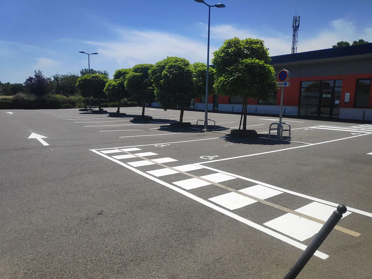 Parking extérieur avec places, flèches, passage piéton, arceaux à vélos et potelets noirs