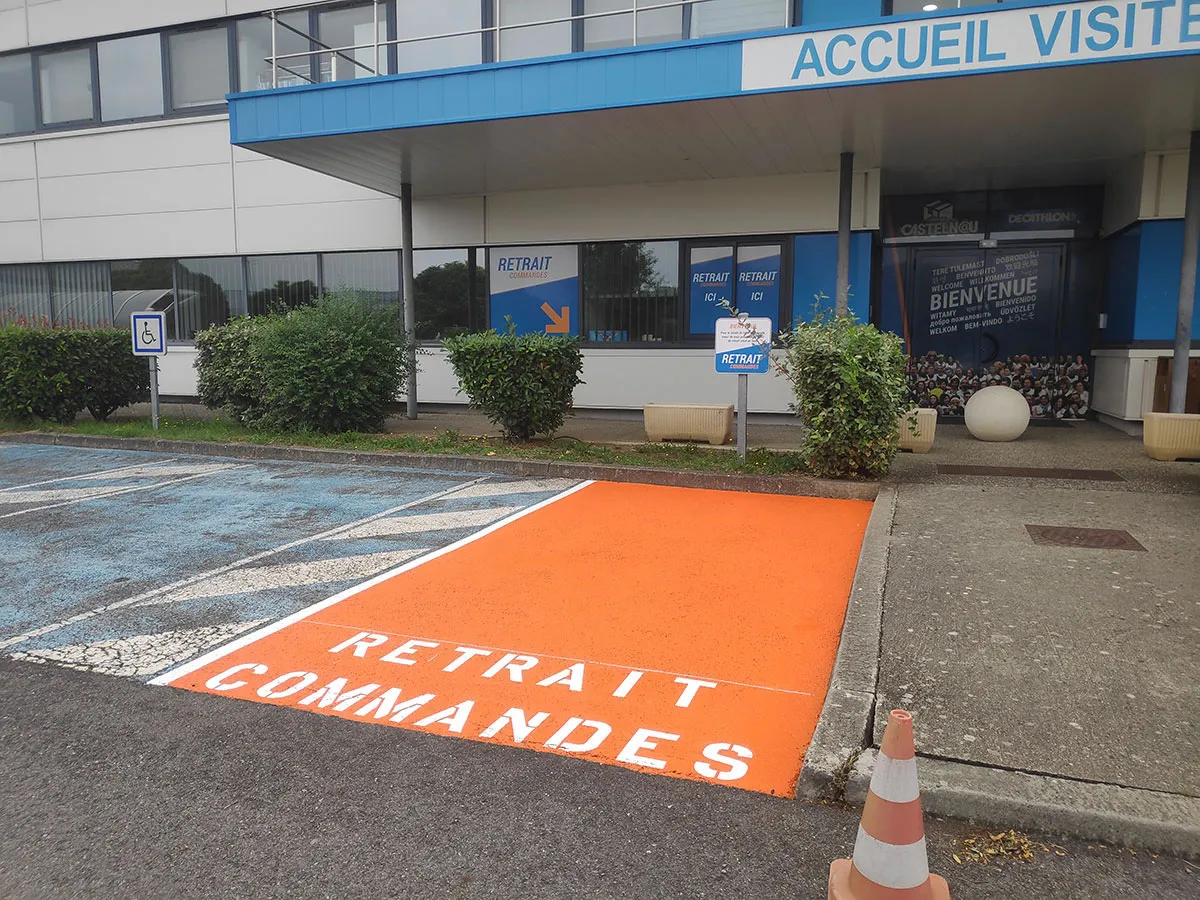 Emplacement orange de retrait de commandes bordé de lignes blanches devant une entrée commerciale