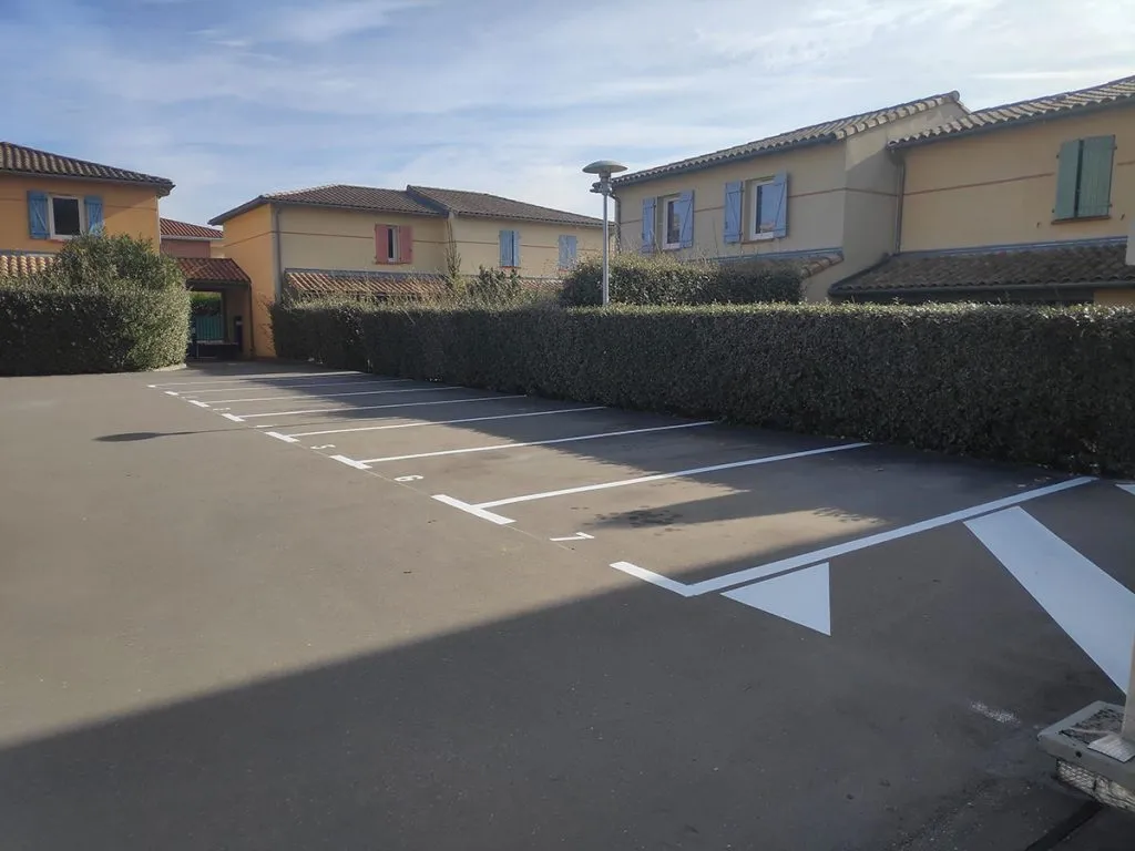 Parking extérieur avec places numérotées, lignes blanches et grande flèche directionnelle