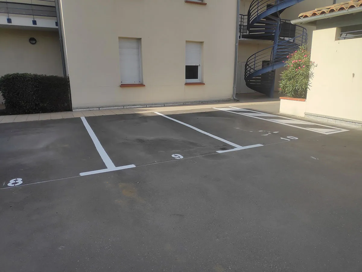 Places de stationnement numérotées et délimitées par des lignes blanches devant un bâtiment
